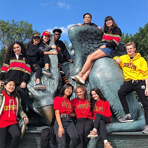 Eleven U of G students sitting and standing in front of and on top of the Gryphon statue
