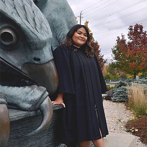 female student wearing graduation gown standing in front of the Gryphon statue