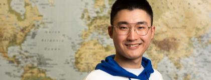 person smiling standing in front of world map