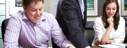 2 co-op students sit at a table, while employer points out something on a document.