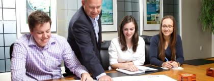 Three co-op students sit at a table, while employer points out something on a document.