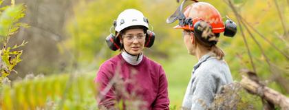 two people talking in nature wearing hard hats