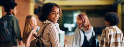Young female high school student walking down the hall with friends.