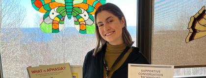 Bio-Med Grad Emily stands in front of a window with her speech pathology materials.