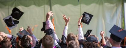 A group of graduates wearing gowns throw their caps in the air in celebration.
