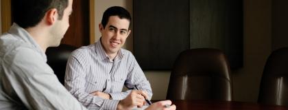 Two people in conversation at a board room table in an office.
