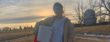 Grad Kathryn Knowles standing in a farm field doing work in an apiary.