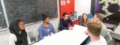 Group of math students sitting around a table and smiling in MacNaughton math study space