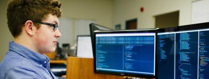 Person looks at two computer screens, with code on them.